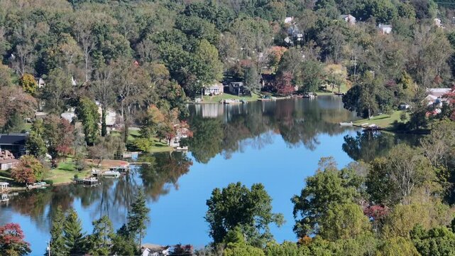 Aerial establishing shot of idyllic Timber lake with Houses during autumnal day. Sunny day in beautiful landscape. Wide shot.
