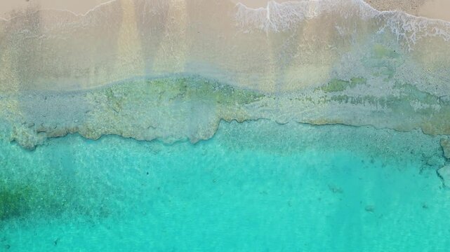 Top-down drone overview of clear turquoise water crashing on golden sand beach, serene nature backdrop