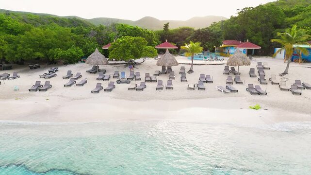 Aerial trucking pan along white sandy beach and turquoise waters at Grote Knip or Playa Abou, Curacao, surrounded by lush greenery and clear blue skies
