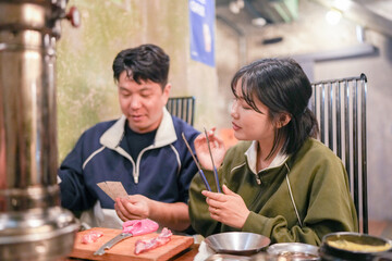 A Korean couple, a man in his 30s and a woman in her 20s, are having a friendly dinner at a samgyeopsal restaurant in Seoul, South Korea.