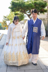 Naklejka premium A Korean couple, a man in his 30s and a woman in her 20s, walk harmoniously on a public road wearing Hanbok in Seoul, South Korea.
