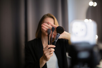 Beauty blogger recording video for her blog, holding makeup brushes.