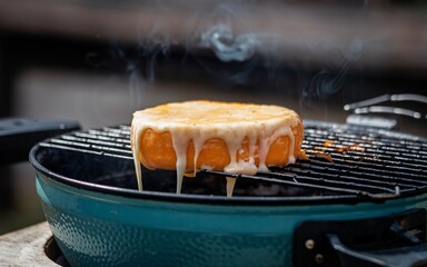 Cheese A round of cheese is grilling on a small charcoal grill, with melted cheese dripping down the sides.