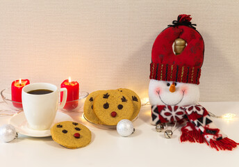 Christmas composition with homemade deer cookies, funny snowman, cup of coffee and lit candles on white table. Home comfort of winter holidays. Empty space for text, blank, greeting card, mock up