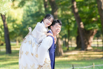 Fototapeta premium A Korean couple, a man in his 30s and a woman in her 20s, are wearing Hanbok and hugging each other in a park surrounded by green trees in Seoul, South Korea.