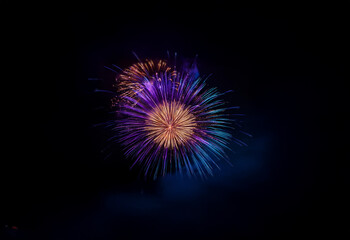 Fototapeta premium A burst of fireworks explodes against a dark, isolated background, displaying vibrant hues of purple, blue, and orange.