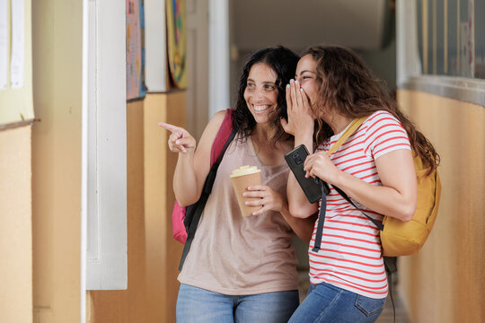 Young girls talking badly about a classmate or co-worker. Concept of talking bad about someone, laughing at someone, evil, bullying. Two friends gossip and are surprised about what they are seeing.