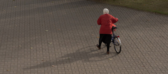 an elderly woman in a headscarf walks next to her bicycle