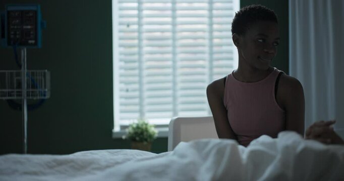 A young African dinka in a hospital room sits next to a patient who is lying in a hospital room and being treated.