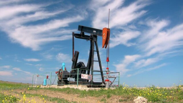 Oil pumpjack in a rural landscape under a bright blue sky with scattered clouds, representing energy production and industry. Ideal for themes of oil, energy, and nature.