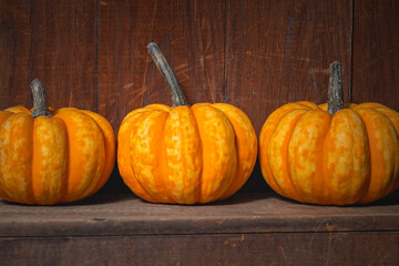 Three bright orange and yellow gourds sit on an old wooden shelf