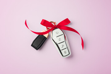 Car key with red bow ribbon on pink background