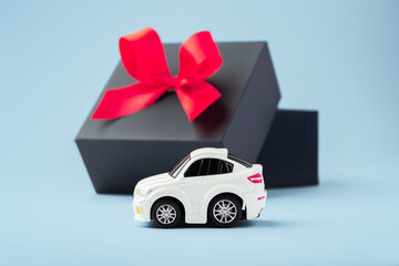 Car toy and black gift box opened with red bow on blue background