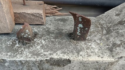 Two rusty metal pieces sticking out of a concrete surface.