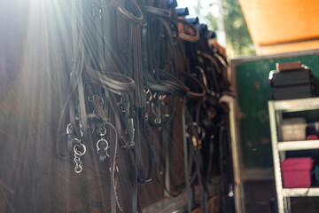 Close-up of horse saddles and harnesses hanging on the stable wall at sunset