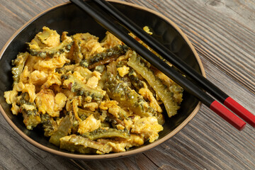 Homemade bitter melon stir-fry with eggs in a bowl. Chopsticks on the bowl.