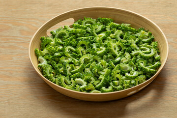 Bitter melon chunks prepared to cook or fry on a bamboo tray. Wooden background.