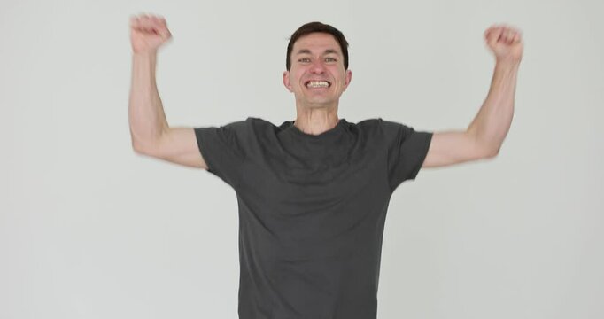 Happy man raises arms in air smiling on white background. Guy radiates joy and excitement capturing moment of celebration triumph slow motion