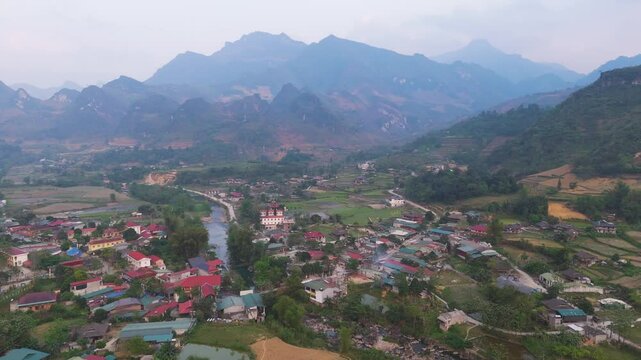 A peaceful aerial view of L&agrave;ng Cắc, showcasing the village's tranquil charm and the river winding through its heart. Motorcycles add a sense of movement to the serene landscape.