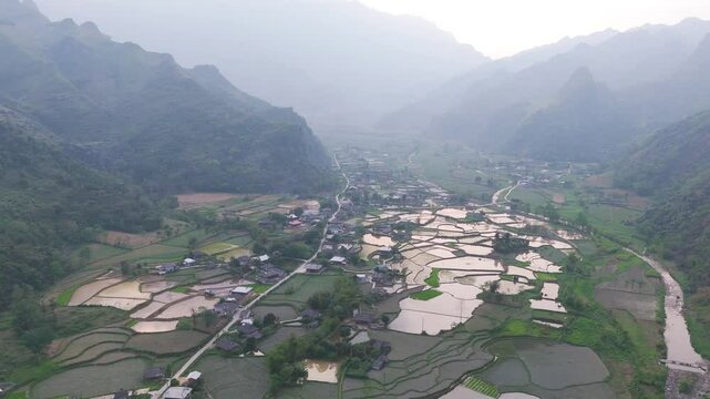 A peaceful aerial view of L&agrave;ng Cắc, showcasing the village's tranquil charm and the river winding through its heart. Motorcycles add a sense of movement to the serene landscape.