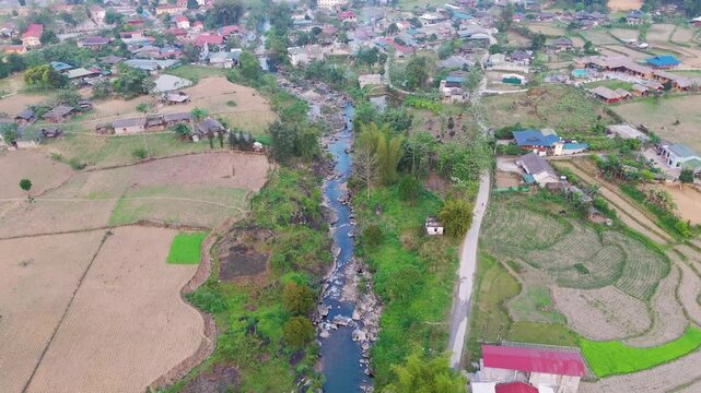 A peaceful aerial view of L&agrave;ng Cắc, showcasing the village's tranquil charm and the river winding through its heart. Motorcycles add a sense of movement to the serene landscape.