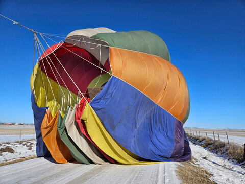 The fabric of a multi colored hot air balloon billows after the balloon lands and the parachute in the top of the balloon is pulled out to help the balloon deflate faster.