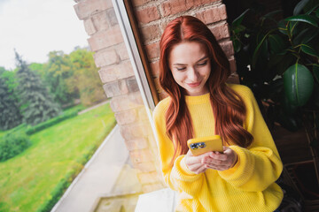 Photo of pretty young woman hold smart phone window wear yellow pullover loft interior apartment...