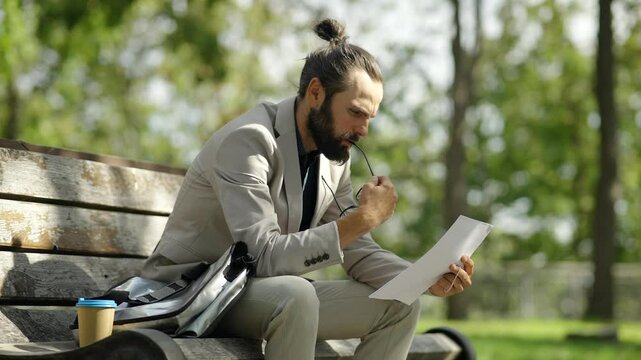 Stressed businessman sitting on bench in park after job loss	