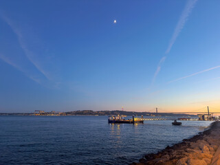 View of the Tagus River in Lisbon with 25 de Abril bridge and Cristo Rei at the end of the day with sunset light.