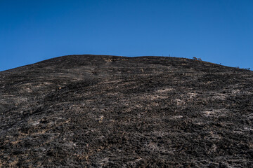 Scorched hill under clear blue sky with barren terrain.