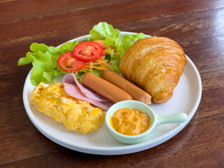Croissants with stuffing in a plate on a wooden dining table. croissant with chicken sausage, ham, omelet and vegetables,tomato . The concept of breakfast, fast food, snack. side view