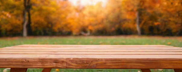 Fototapeta premium Wooden table in an autumn park with vibrant orange foliage in the background.