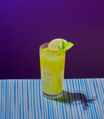 Yellow cocktail garnished with mint and a slice of lemon in a tall glass.