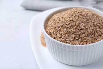 Buckwheat bran in bowl on light grey table, closeup