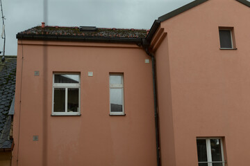There is a pinkcolored building adorned with two windows and featuring a charming chimney situated prominently on the roof