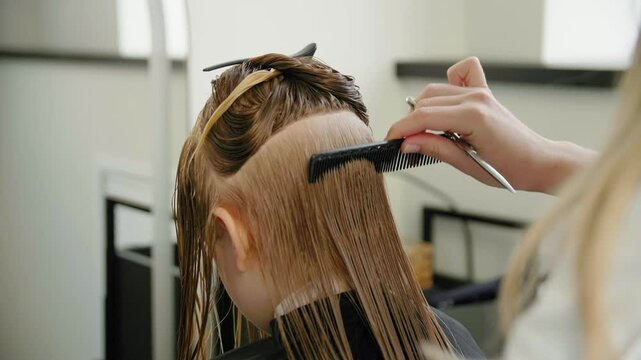 Close-up of hairstylist's hands combing girl's wet hair at the hair salon. First haircut.