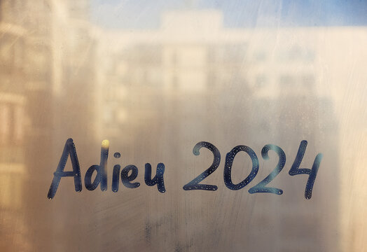 lettering adieu in French is goodbye in english and numbers 2024 is twenty twenty-four paint with finger on splashed by rain foggy glass sunset window