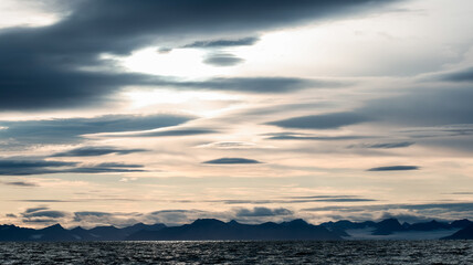 Cloudy skies over the serene landscape of Svalbard\'s coastal waters at dusk