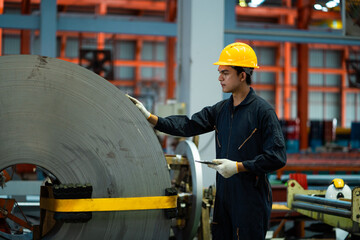 A man in a yellow and black safety suit is working on a large piece of metal. He is wearing a yellow safety harness and a yellow safety belt