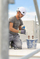 Craftsman in grey work clothes puts grout on a float sitting on his knees during construction