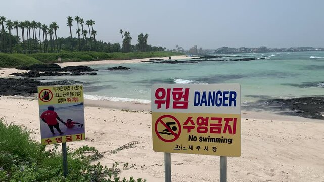  Information sign about the quicksand at beach. No swimming, danger zone. Motion of Yellow sea waves. Black Volcanic rocks inside the water. Hyeopjae Beach, South Korea