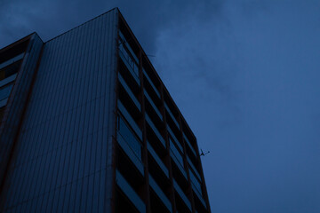 As I gaze upward at a magnificent tall building illuminated at night, the beautiful blue sky serves as a stunning backdrop to the scene