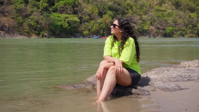 Wide Shot of Indian Woman Sitting Near Ganga River and Looking Around, Rishikesh