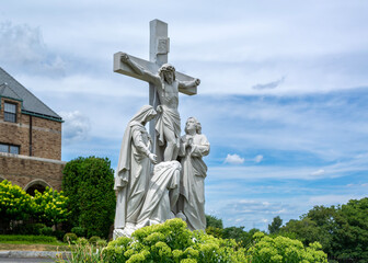 Crucifixion Statue Amidst Greenery at St. Columbkille Church against cloudy sky in Brighton, Massachusetts, USA