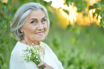 Portrait of a beautiful elderly woman with a bouquet of flowers in the park