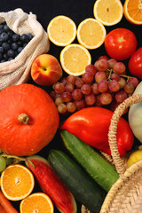 Round straw bag and various seasonal fruits and vegetables on dark background. Summer and fall produce. Top view.