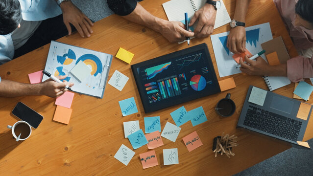 Executive manager explain financial graph to colleague at meeting room. Top aerial view of diverse marketing team sharing idea and planning strategy while sitting at table with tablet. Convocation.