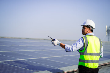 A man in a yellow vest is standing on a solar panel. He is holding a remote control and wearing a...