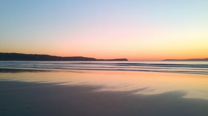Fototapeta premium A tranquil sunrise over a calm ocean with a sandy beach in the foreground.