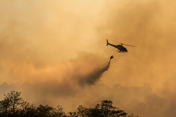 Fire fighting helicopter carry water bucket to extinguish the forest fire.